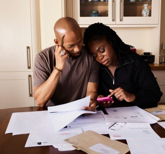 Casal analisa documentos e administra as finanças domésticas enquanto usa um smartphone à mesa.