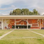 Edifício contemporâneo com mural colorido na fachada, cercado por gramado.