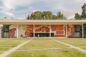 Edifício contemporâneo com mural colorido na fachada, cercado por gramado.