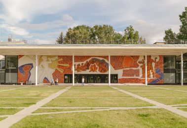 Edifício contemporâneo com mural colorido na fachada, cercado por gramado.