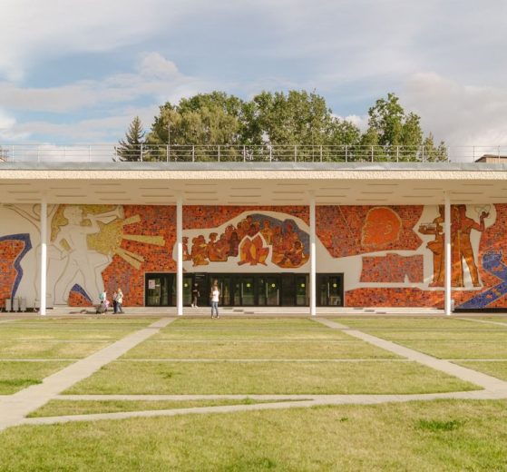 Edifício contemporâneo com mural colorido na fachada, cercado por gramado.