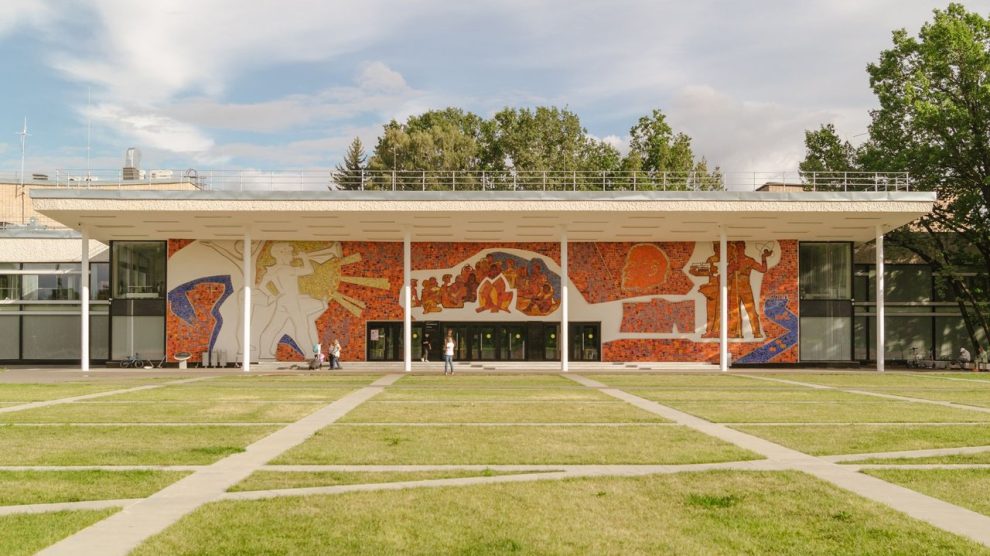 Edifício contemporâneo com mural colorido na fachada, cercado por gramado.