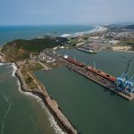 Vista aérea do Porto de Imbituba, com docas, guindastes, navios e a costa brasileira.